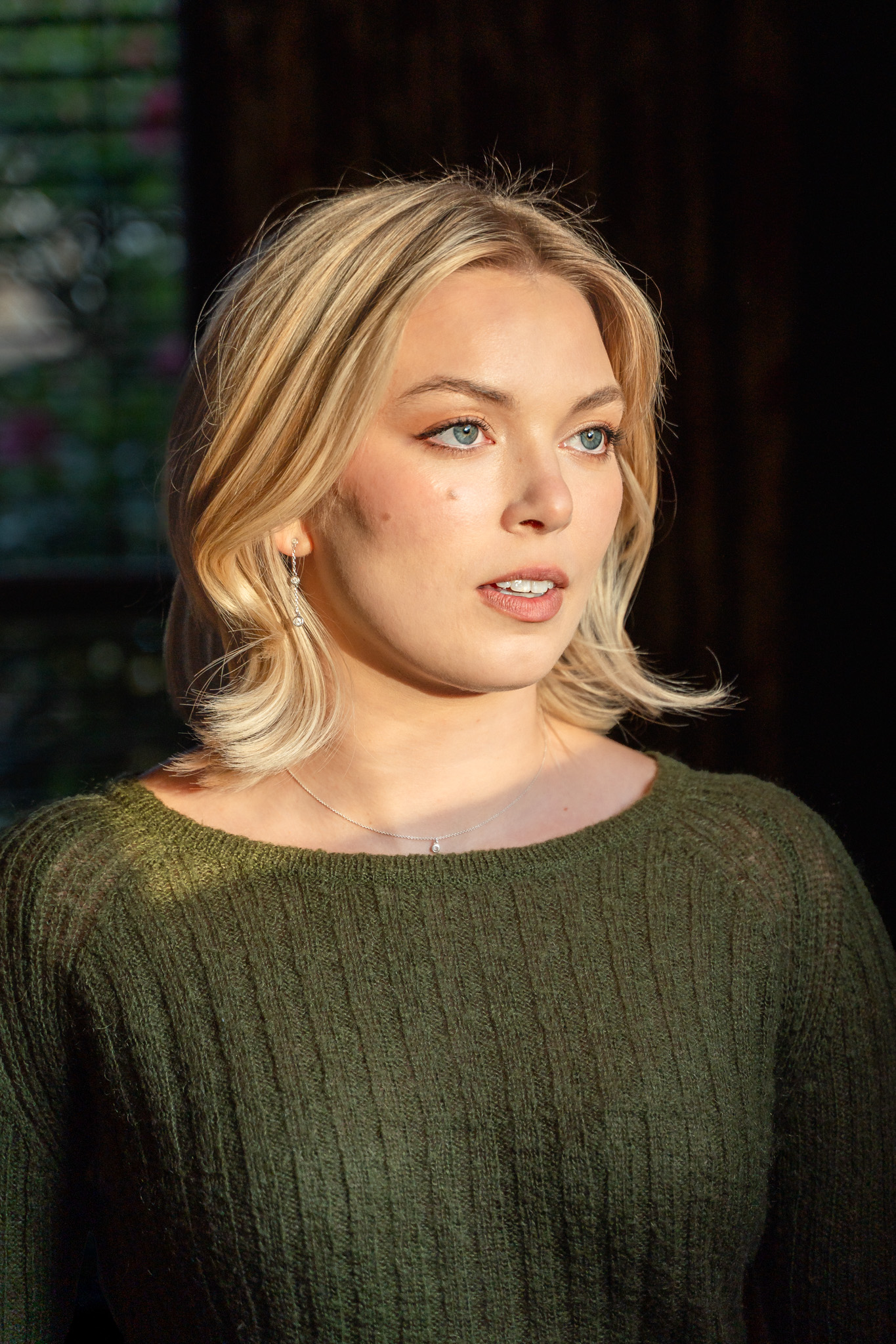 woman, blonde hair hazel eyes looking out window, green knit sweater, natural light